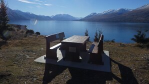 A picnic table with benches overlooking a calm lake with mountains in the background.
