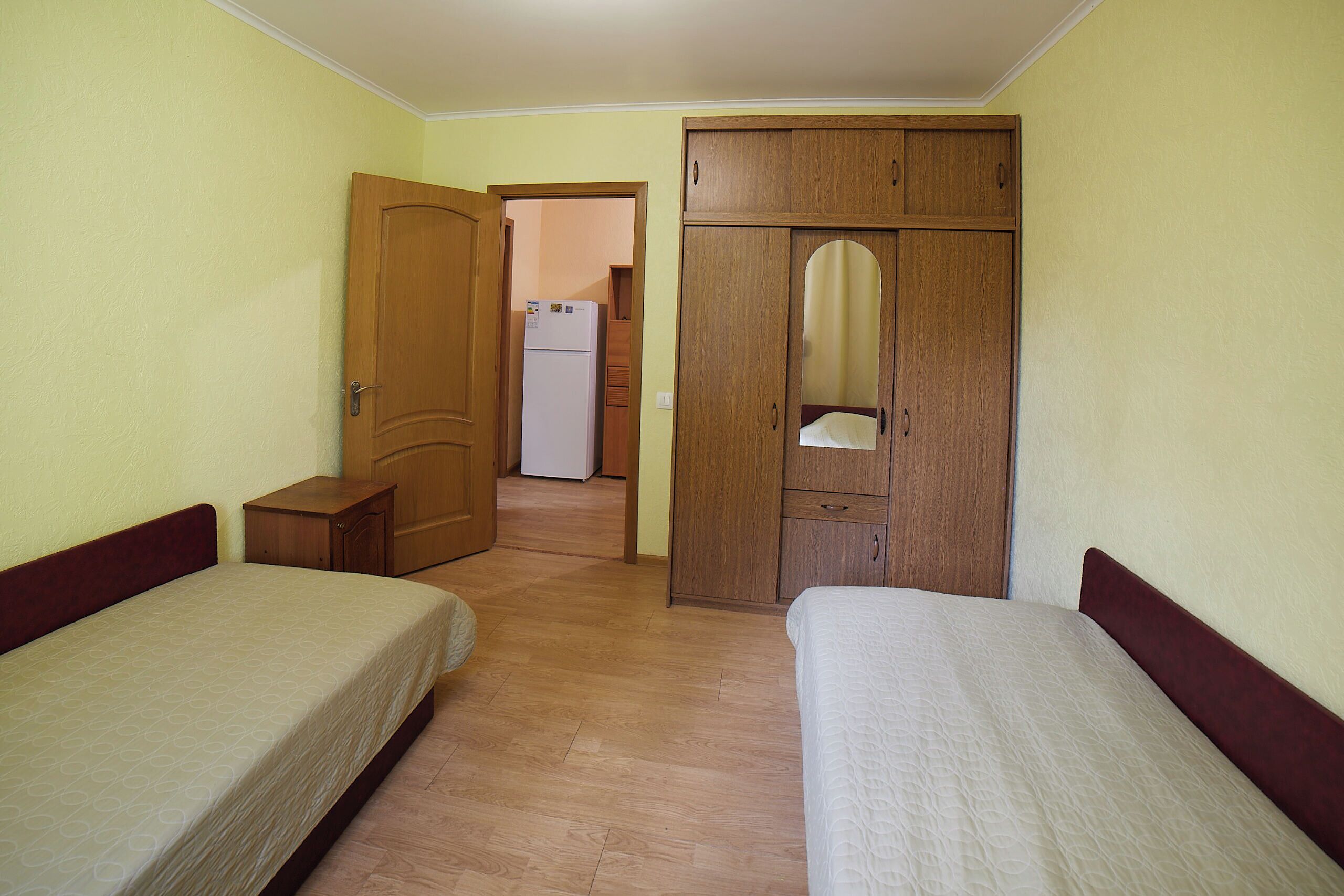 A bedroom with two beds, wooden wardrobe, and a small cabinet.