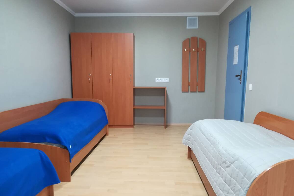 A room with two single beds, a wardrobe, a small table, and a blue door.