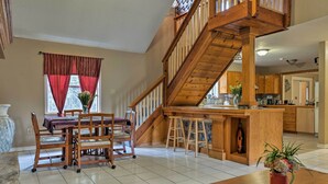 A spacious living area with a wooden staircase, a dining table with chairs, and a kitchen area in the background. - Dripping Springs Home w/ Deck, Near Wedding Venue (Dripping Springs)