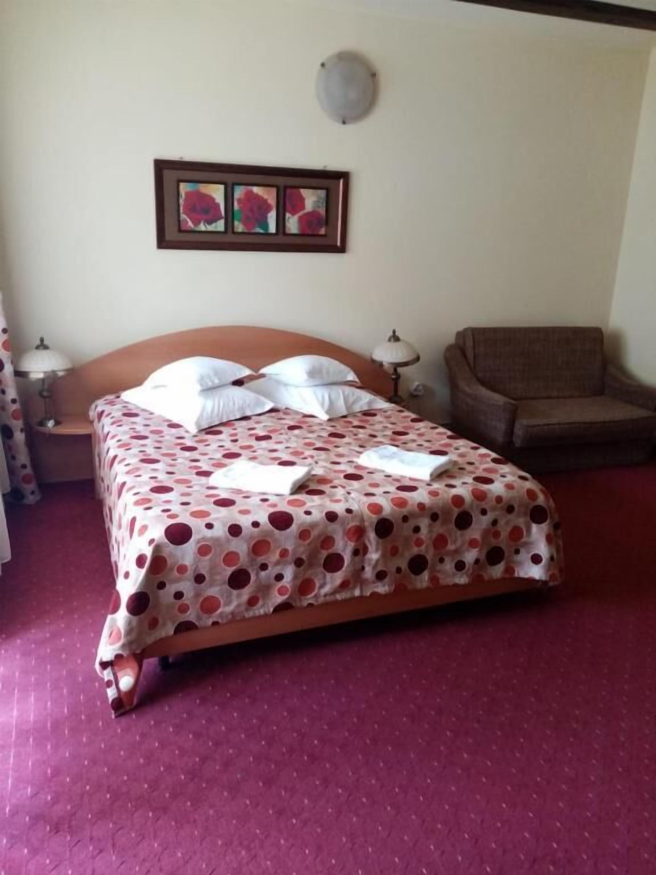A bedroom with a bed, a chair, a nightstand, and a wall clock.