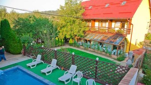A pool area with lounge chairs and a table, surrounded by a wooden fence and greenery. - Casa Bazna (Bazna)