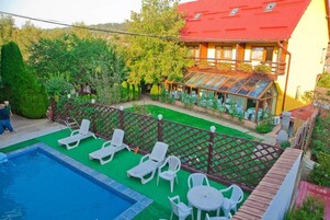 Un área de piscina con sillas de descanso y una mesa, rodeada por una valla de madera y follaje.