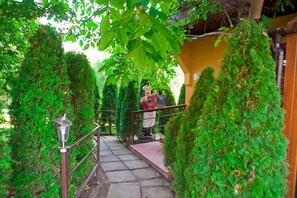 A stone staircase with metal railings, surrounded by lush green foliage and a statue of a chef. - Casa Bazna (Bazna)
