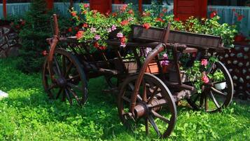 A wooden cart with flower boxes, surrounded by greenery and a red building in the background.