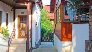 A narrow alleyway with a wooden staircase leading to a door, surrounded by buildings with wooden facades and a green fence in the background. - Casa Bazna (Bazna)