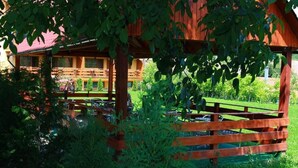 A wooden gazebo with a red roof, surrounded by lush greenery and a wooden fence. - Casa Bazna (Bazna)