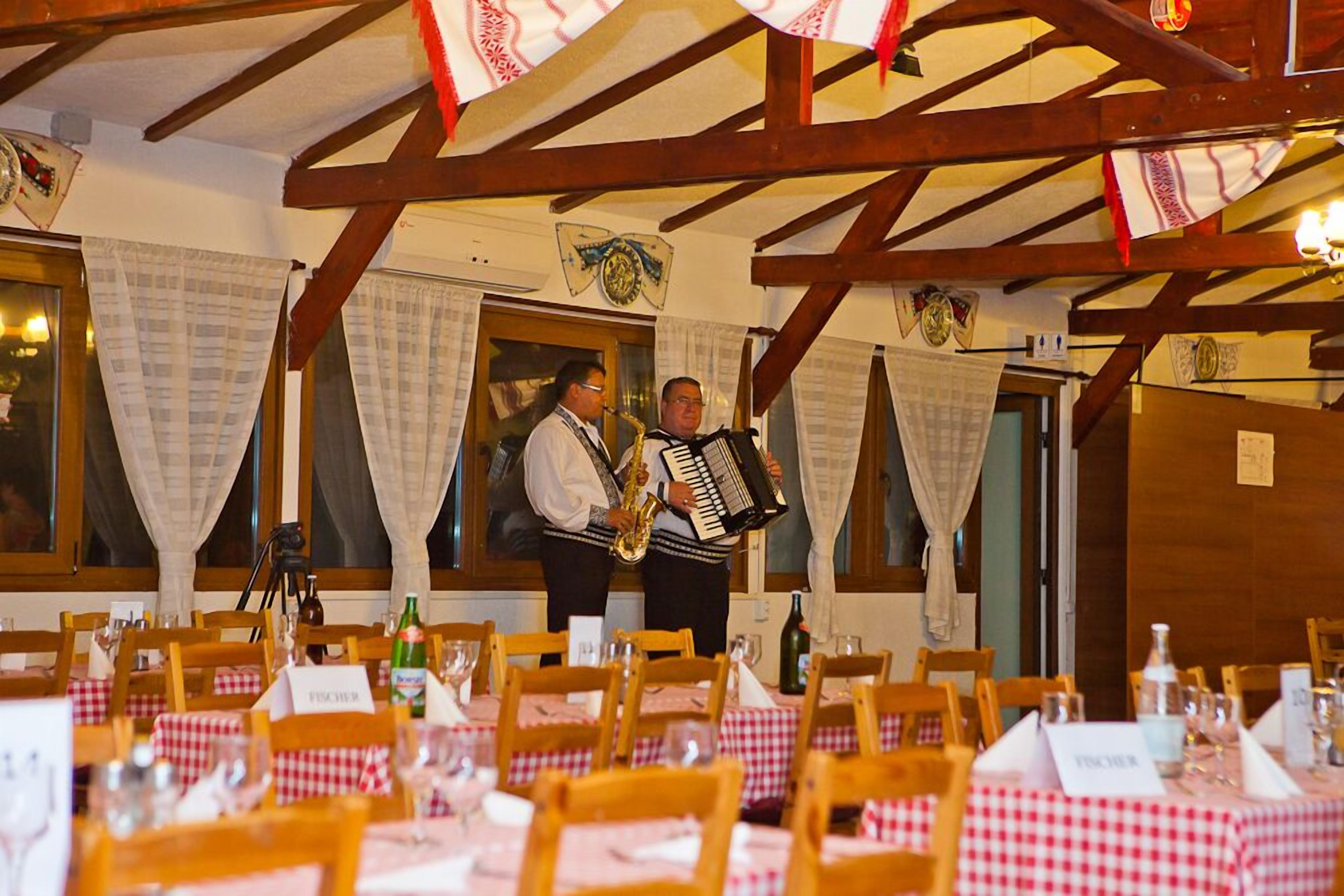A restaurant with wooden beams, checkered tablecloths, and a saxophonist playing.