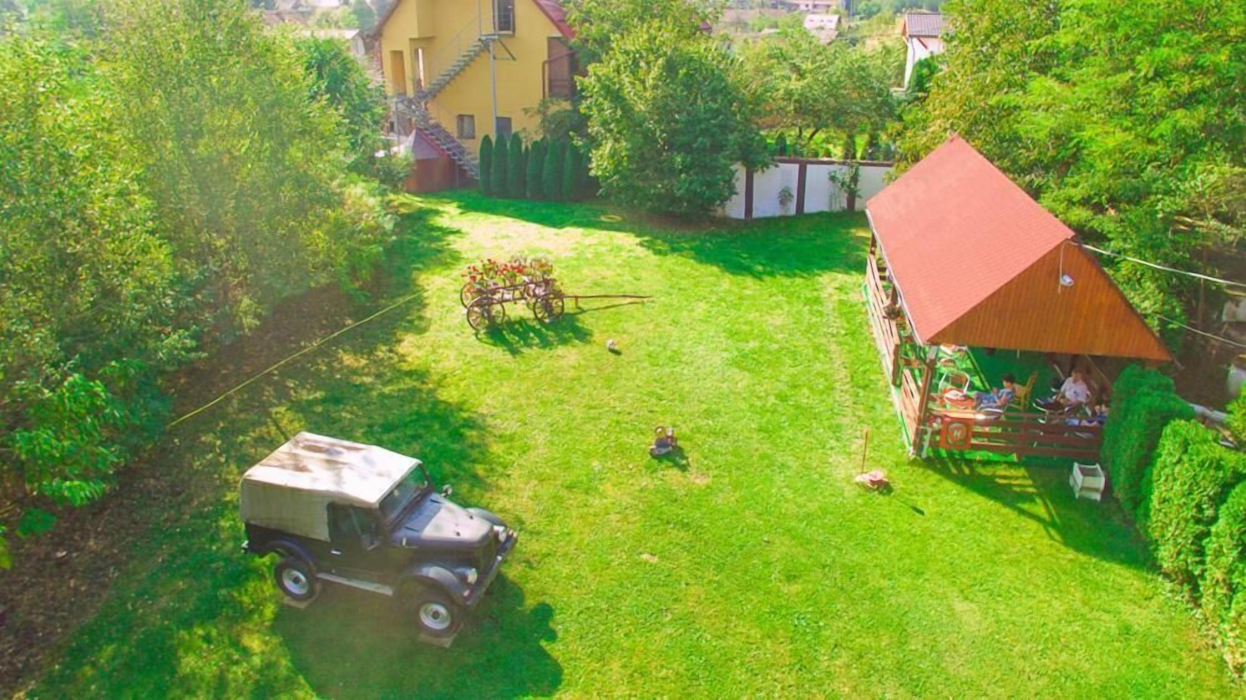 A rural setting with a yellow house, a red-roofed barn, and a vintage truck parked on a grassy area.