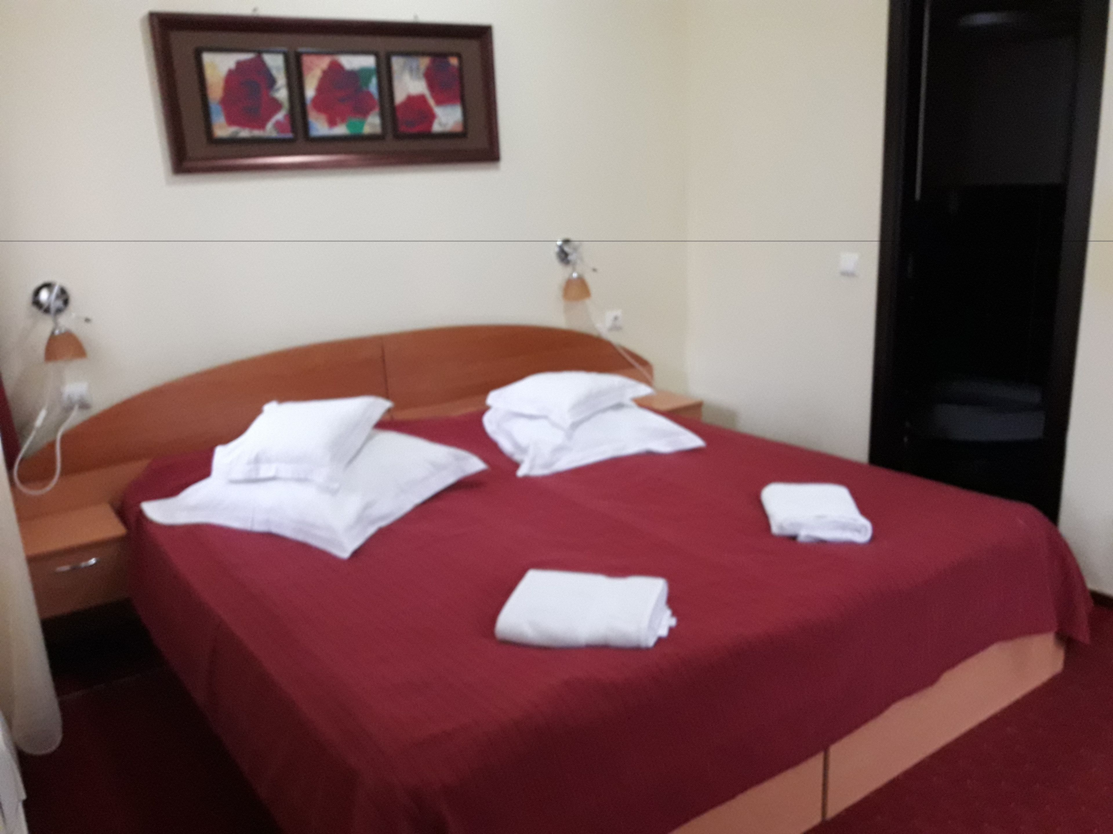 Een hotelkamer met een bed, een nachtkastje, een lamp en een kunstwerk in een lijst aan de muur.
