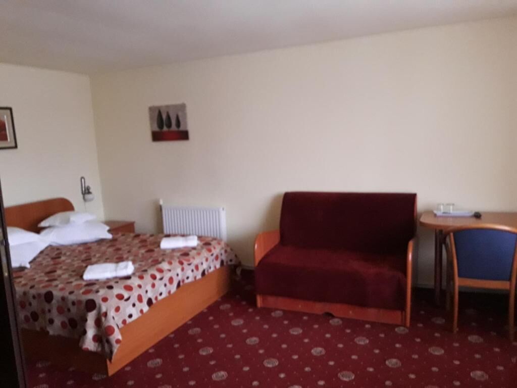 A hotel room with a bed, a red sofa, a small table, and a radiator.