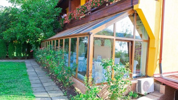 A conservatory with glass walls, a wooden balcony, and a garden path. - Casa Bazna (Bazna)