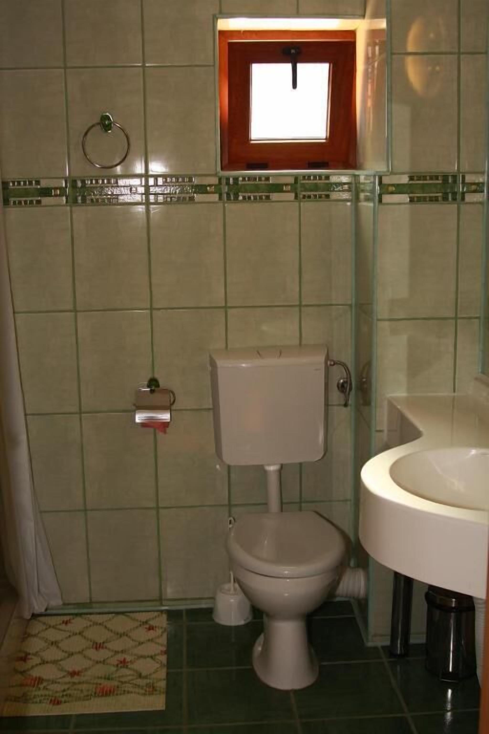 A small bathroom with a toilet, sink, and a window above the toilet.