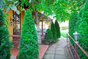 A pathway leading to a building with a covered porch, surrounded by neatly trimmed hedges and trees. - Casa Bazna (Bazna)