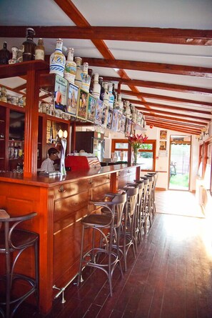 A bar area with wooden beams, a counter with stools, and shelves with bottles and framed pictures. - Casa Bazna (Bazna)
