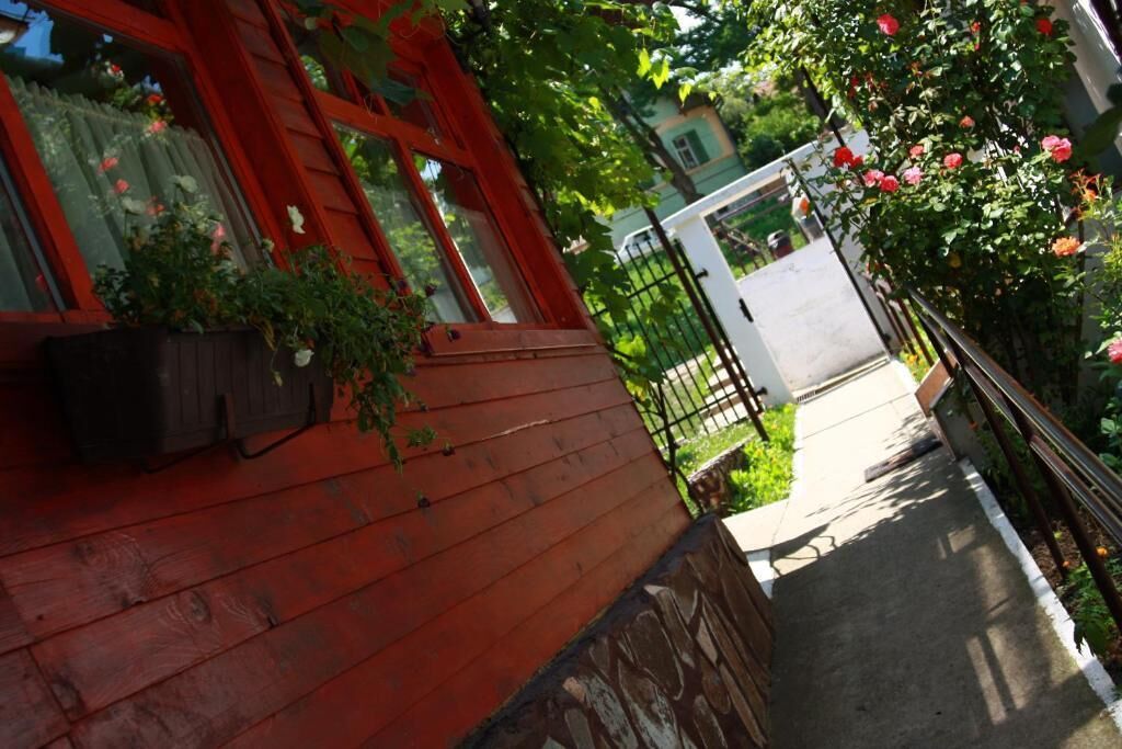 A wooden house with a red exterior, a stone foundation, and a garden with roses.