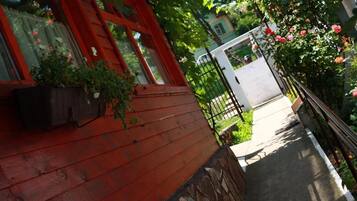 A wooden house with a red exterior, a stone foundation, and a garden with roses.