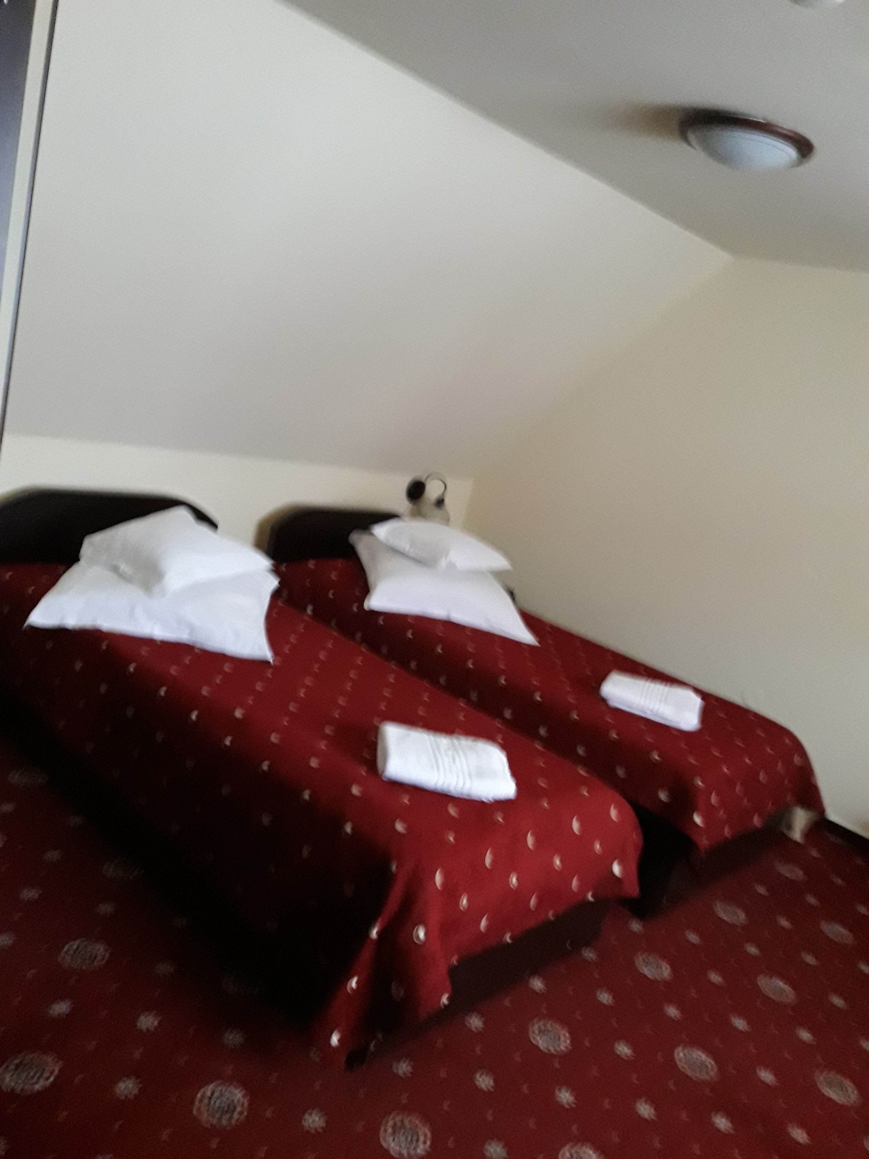 A hotel room with two beds, each with white pillows and a red bedspread with a pattern.