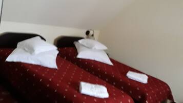 A hotel room with two beds, each with white pillows and a red bedspread with a pattern.