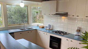 A modern kitchen with a curved island, white cabinets, a gas stove, and a large window with a view of greenery. - Jan Juc Beach Break - Walk to Beach, Pet Friendly (Jan Juc)