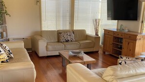 A living room with a wooden ceiling, a beige sofa, a wooden coffee table, and a TV mounted on the wall. - Jan Juc Beach Break - Walk to Beach, Pet Friendly (Jan Juc)