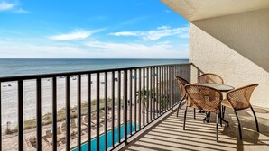 Varanda com vista para a praia e oceano, cadeiras de vime e piscina.