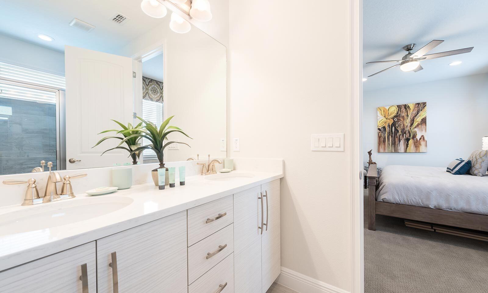 A modern bathroom with a large mirror, white cabinetry, and a plant.