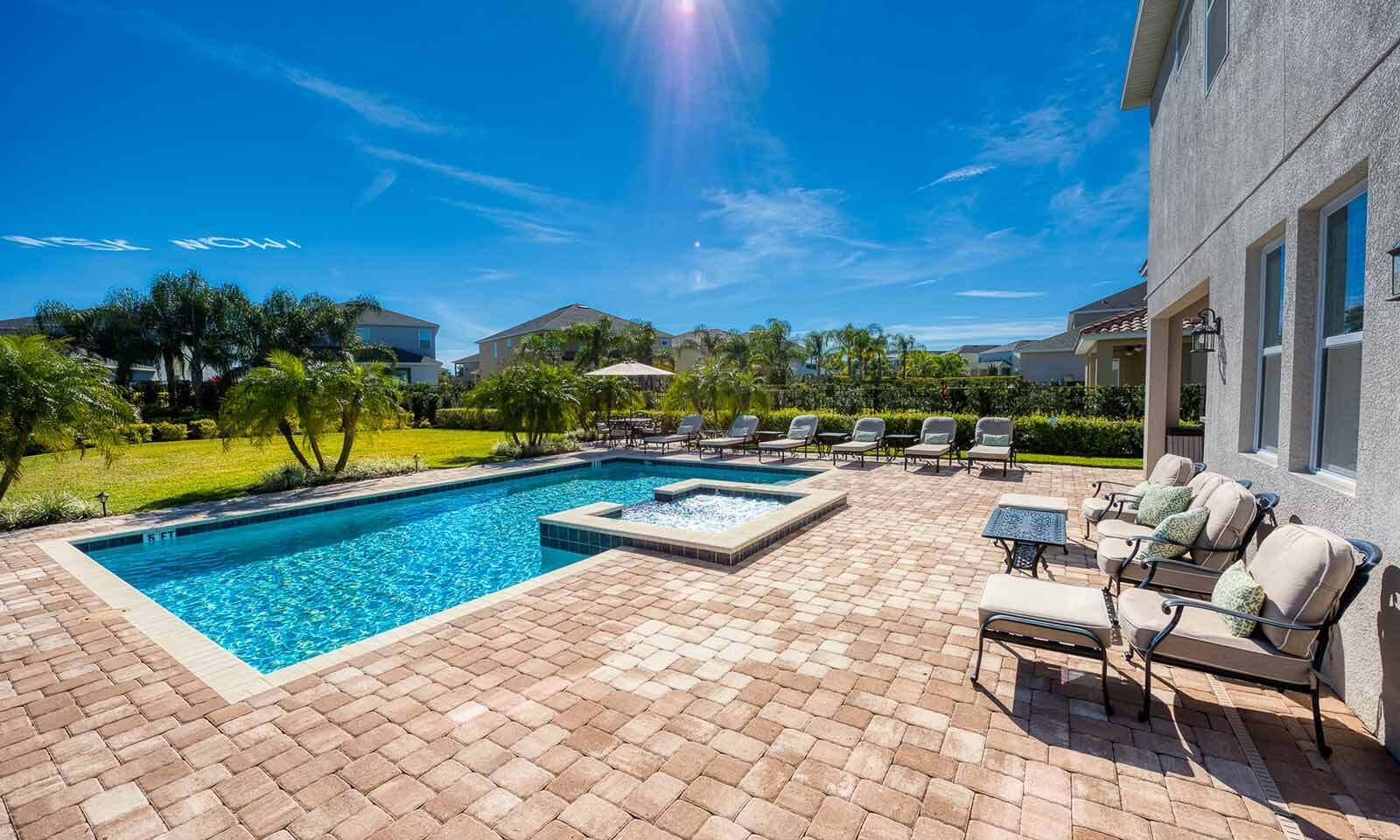A swimming pool with a hot tub, surrounded by a patio with lounge chairs and a table.