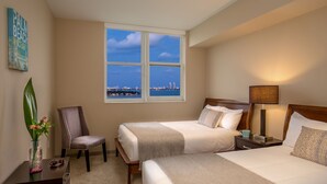 A hotel room with two beds, a chair, a nightstand, a lamp, a vase with flowers, and a window with a city view. - Shorecrest Miami Bay (Miami)