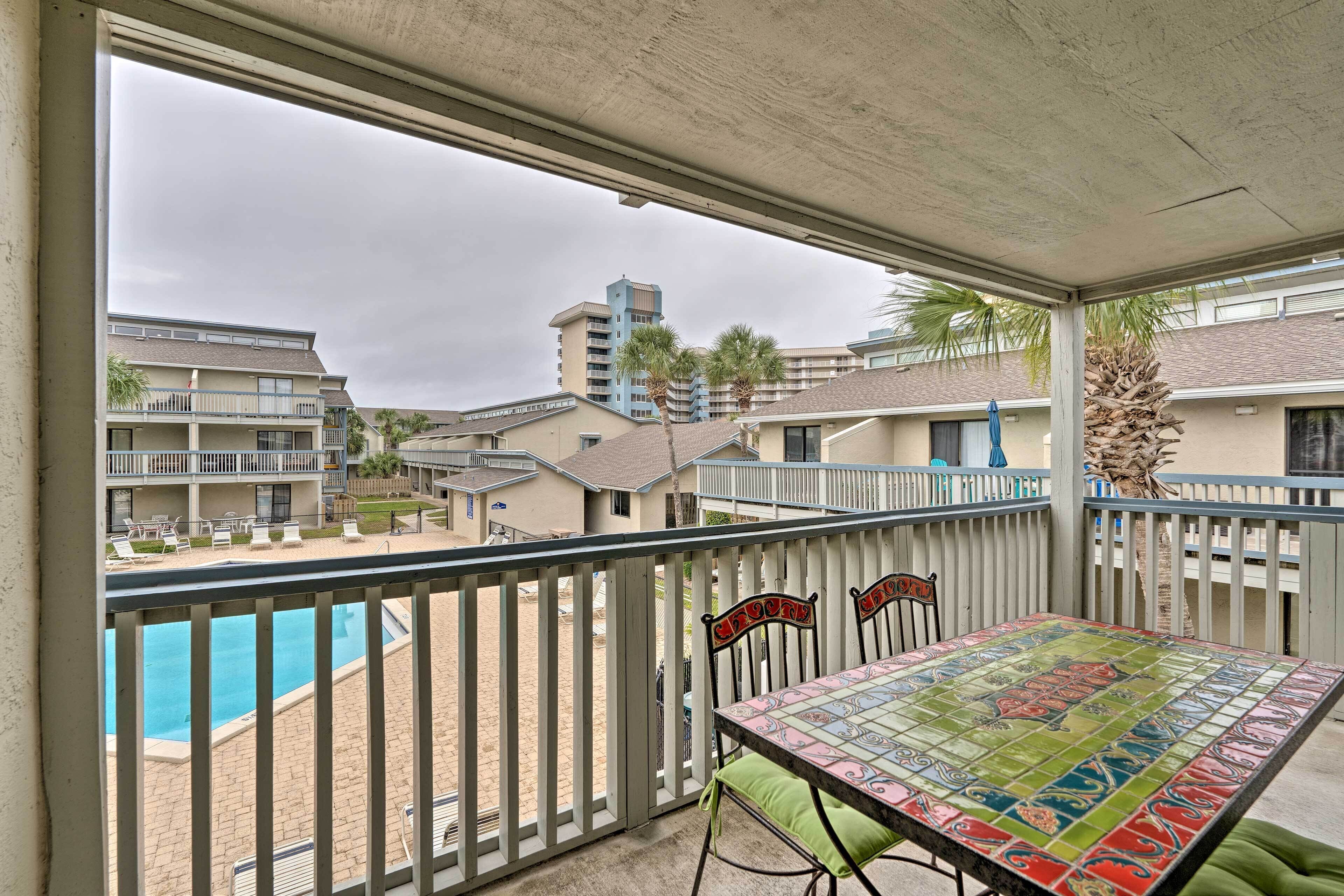 Uma varanda com vista para uma piscina, uma mesa com cadeiras e uma palmeira.