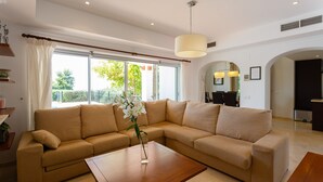 A modern living room with a beige sectional sofa, a wooden coffee table, and a large window with curtains.
