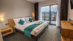 Hotellihuone, jossa on sänky, puinen yöpöytä, työpöytä, televisio ja suuri ikkuna, josta avautuu näkymä lumiseen maisemaan.