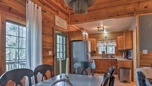 A wooden cabin interior with a dining table, chairs, a chandelier, and a kitchen area. - Ruidoso Log Cabin Retreat - Peaceful & Convenient (Ruidoso)