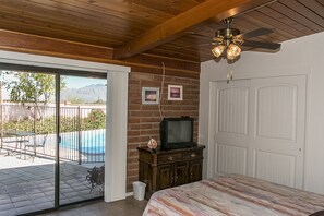 A bedroom with a wooden ceiling, a ceiling fan, a TV on a wooden cabinet, a bed, and a sliding glass door leading to a pool area. - Beautiful home with pool, private, close to UA & Downtown, arts. Great prices! (Tucson)