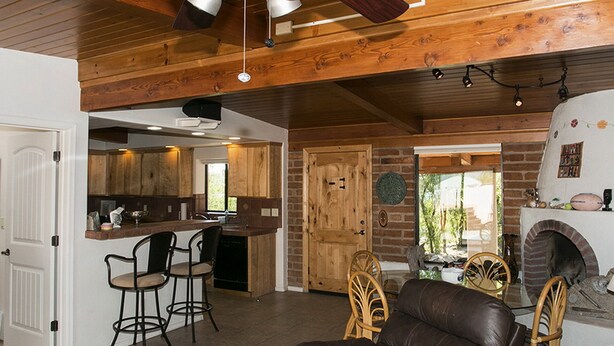 A rustic interior with a wooden ceiling, a kitchen area, a seating area with a leather couch, and a fireplace. - Beautiful home with pool, private, close to UA & Downtown, arts. Great prices! (Tucson)