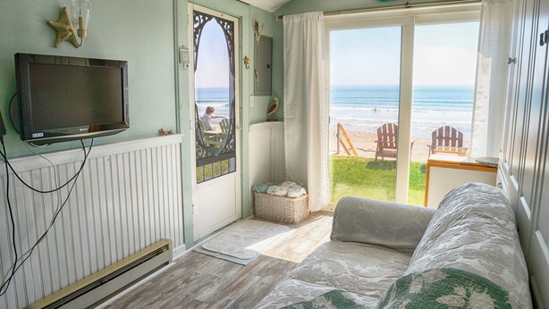 A cozy room with a television, a view of the beach, and a comfortable seating area. - Moody Beach Front Studio Cottage WIFI (Wells)