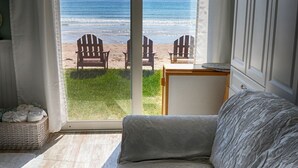 A room with a large sliding glass door leading to a beach view, a sofa, and a small table. - Moody Beach Front Studio Cottage WIFI (Wells)