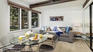 Una sala de estar moderna con una mesa de comedor de vidrio, sillas de metal, un sofá gris y un cuadro en la pared.