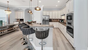 Une cuisine moderne avec des meubles blancs, des appareils en acier inoxydable et un îlot central doté de tabourets de bar.