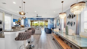 Une cuisine moderne dotée d’un coin bar, d’un ventilateur de plafond et d’un espace repas avec une table en verre et des bancs.