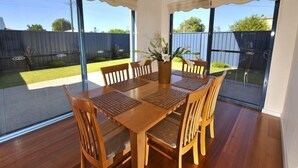 A dining area with a wooden table and chairs, a vase with flowers, and large sliding glass doors leading to a backyard. - Palm Beach Manor ... (Rockingham)
