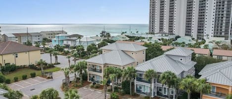 A coastal residential area with a mix of single and multi-story buildings, some with balconies, and a parking lot in the foreground.