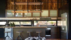 A modern kitchen with wooden cabinetry, a stainless steel refrigerator, and a bar area with stools.