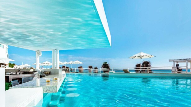 A pool area with clear blue water, white umbrellas, and a view of the ocean. - Enjoy Huge Private Terrace with Hot Tub - Beachfront! (CANCUN)