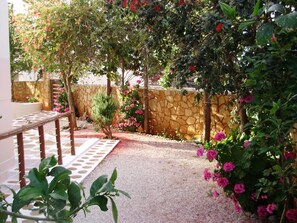 Un jardin avec un mur en pierre, un banc en bois et diverses plantes et fleurs.