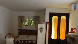 Um quarto com piso estampado, uma cama com cabeceira, uma cadeira, uma mesa com uma tigela e uma lareira.