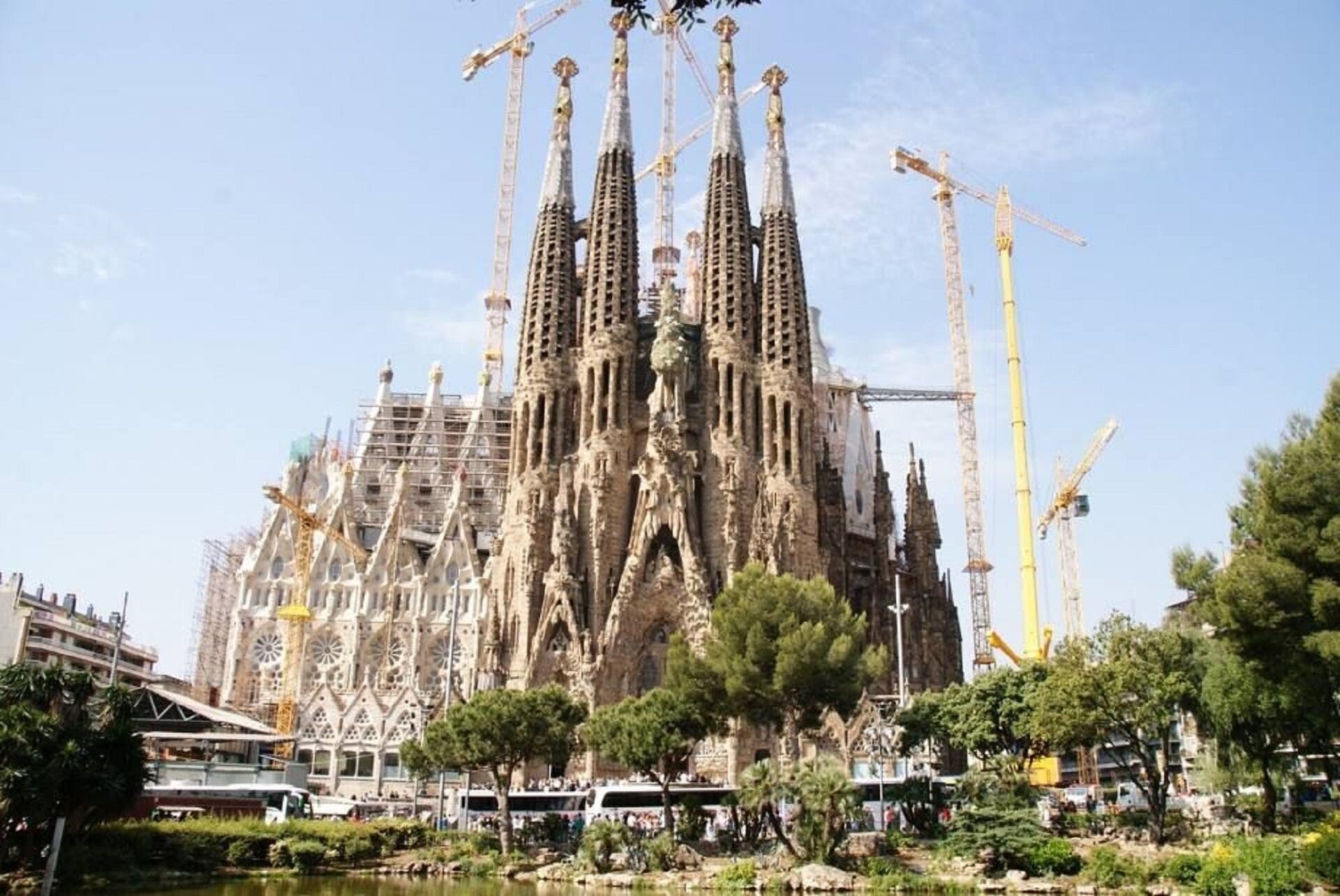 Un edificio grande con múltiples agujas y grúas de construcción, rodeado de árboles y una masa de agua.