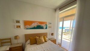Een slaapkamer met een groot bed, een houten hoofdbord en uitzicht op het strand door een schuifdeur.