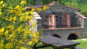 A stone building with a brick chimney, a picnic table, and yellow flowers in the foreground. - Apt. The Nabucco, Casa Lama Residence, 6/8 Persons, ideal for large families (Castelfranco di Sopra)