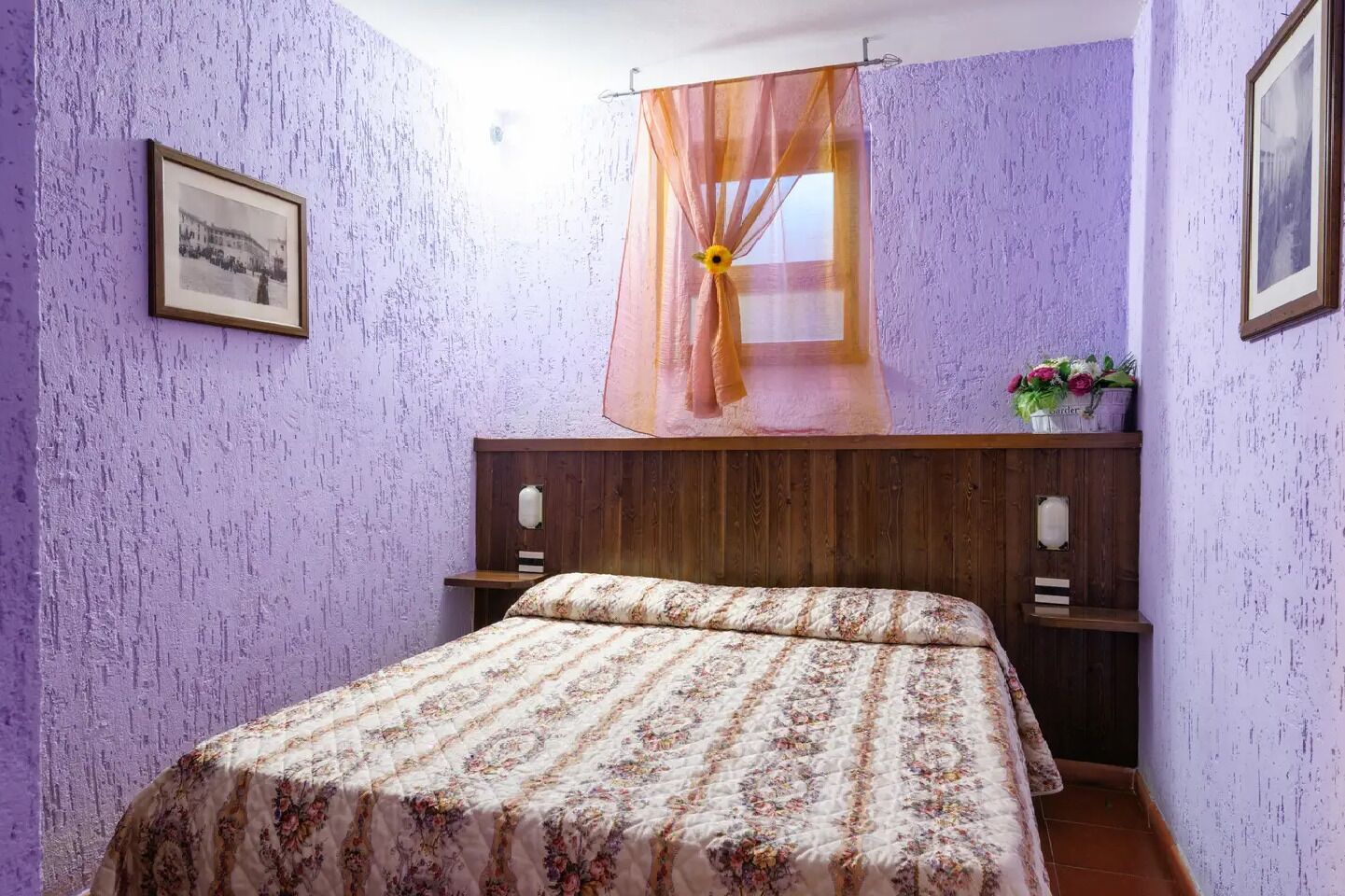 A bedroom with a bed, wooden headboard, purple walls, and a window with sheer curtains.